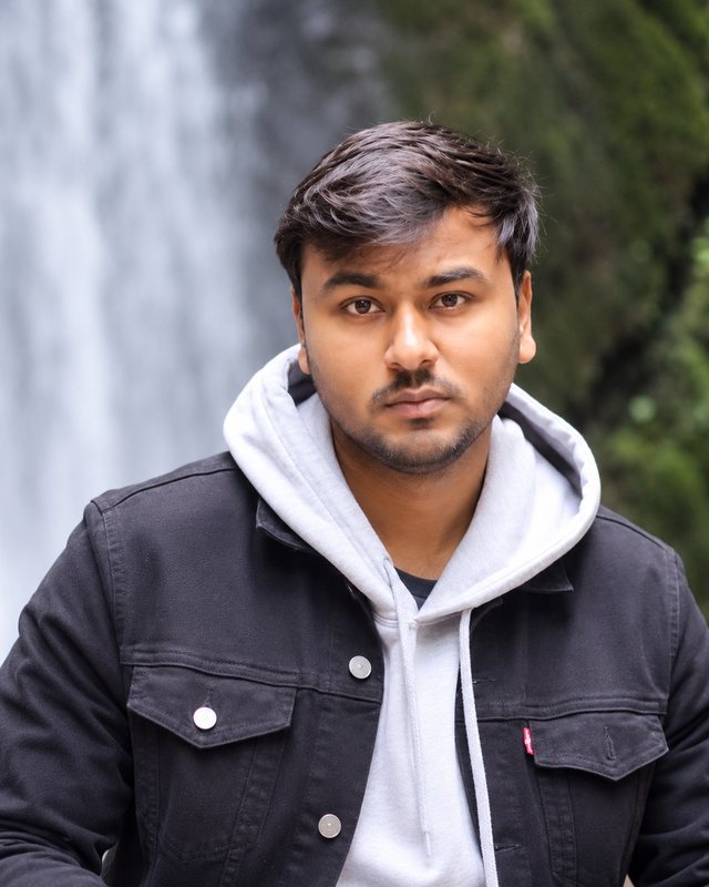 Portrait of Mr. Ritesh Kumar in a dark jacket and grey hoodie, in front of a waterfall